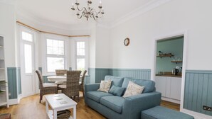 Un salon avec un canapé bleu, des fauteuils en osier, une table basse blanche et un lustre.