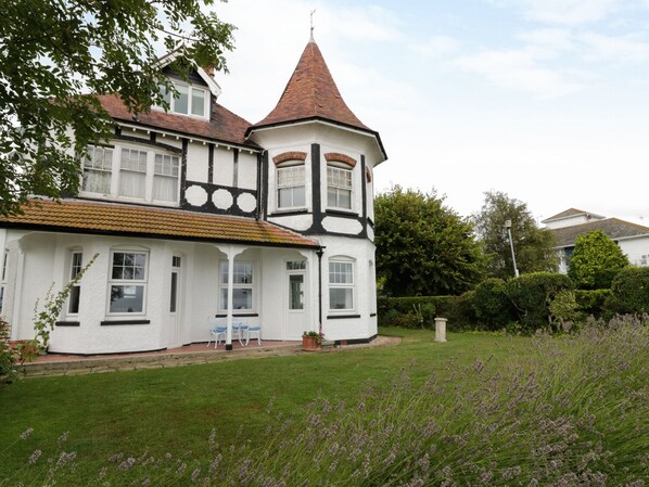 A large, white, Tudor-style house with a prominent tower and a well-maintained garden.