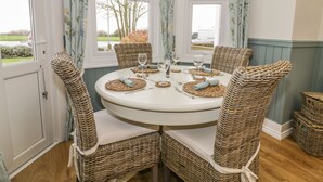 Une table de salle à manger ronde, entourée de quatre chaises en osier, chacune agrémentée d’un coussin. La table est mise avec de la verrerie et des sets de table.