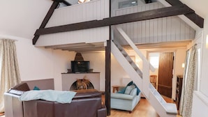 Ett vardagsrum i loftstil med en öppen spis, en soffa, en ljusblå fåtölj och en trappa som leder upp till ett övre plan.