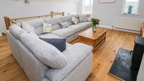 A modern living room with a grey sectional sofa, a wooden coffee table, and a black TV stand. There are skylights and a large window providing natural light. - Mor Awelon (Goodwick)