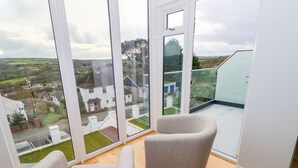A room with large windows offering a view of a residential area. There are two upholstered chairs and a wooden floor. - Mor Awelon (Goodwick)