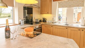 A kitchen with wooden cabinets, a large island, and a window with a view of the outside. - Meadow Cottage (Keighley)
