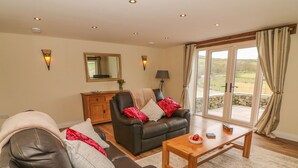 A living room with a leather sofa, a wooden coffee table, and a view through large glass doors to an outdoor area. - Meadow Cottage (Keighley)