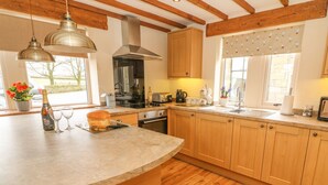 A kitchen with wooden cabinets, a large island, pendant lights, and a view of the outdoors. - Meadow Cottage (Keighley)
