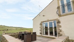 A house with a stone wall patio, a glass door, and a view of the countryside. - Meadow Cottage (Keighley)