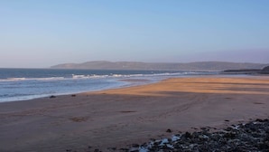 Une plage dotée d’un large rivage sablonneux, de vagues douces et de collines qui se dessinent à l’horizon.