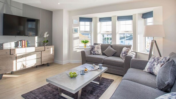 Un salon moderne avec un canapé gris, une table basse et un téléviseur fixé au mur.