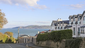 Un quartier résidentiel en bord de mer, avec des maisons modernes, une vue dégagée sur la mer et un mur de pierre menant à un portail.