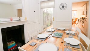 Ein Esszimmer mit Holztisch, gedeckt für vier Personen, weißen Stühlen, einem Kamin und einer Uhr an der Wand.