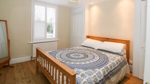 Ein Schlafzimmer mit einem hölzernen Bett, einer gemusterten Bettdecke, einem weißen Heizkörper, einem Fenster mit Jalousien und einer Deckenleuchte.