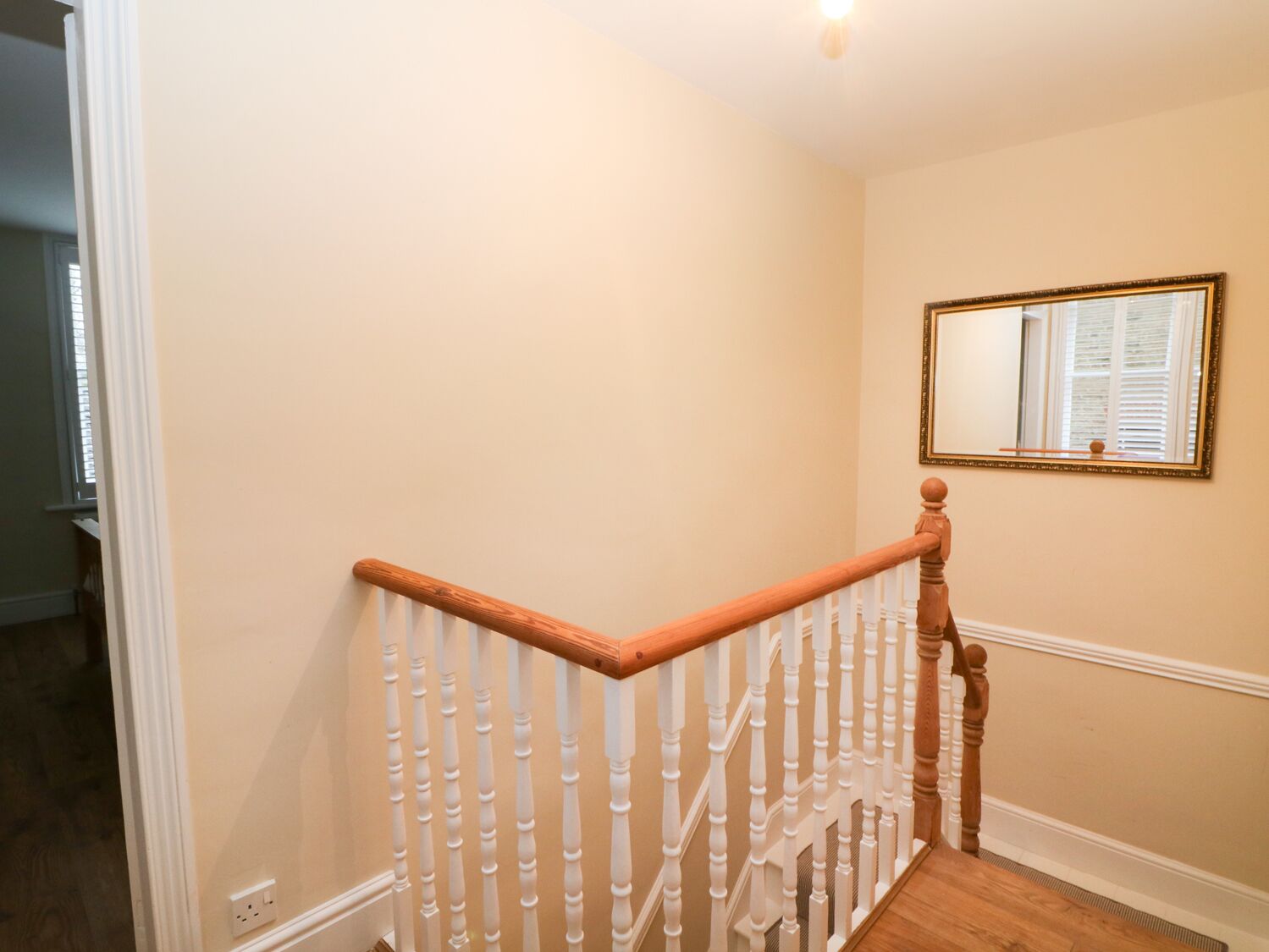 A staircase with white balusters and wooden handrails, leading to a landing with a mirror and a framed picture on the wall.