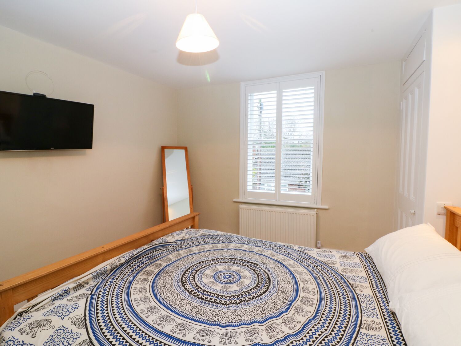 Une chambre à coucher avec un lit, un téléviseur fixé au mur, une fenêtre avec des stores et un miroir.