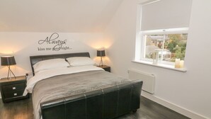 A bedroom with a bed, bedside lamps, a window with a view, and a wall with a message. - 5 Old Laundry Mews (Carnforth)