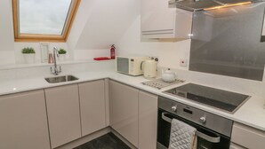 A modern kitchen with a built-in oven, a microwave, and a stovetop. - 5 Old Laundry Mews (Carnforth)