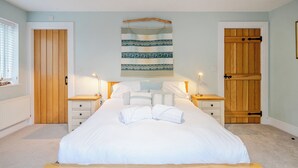 A bedroom with a large bed, two bedside tables, a wall tapestry, and wooden doors. - Curragho (Holyhead)