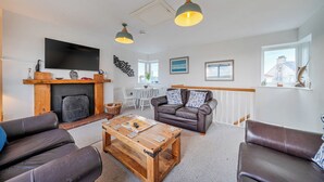 A living room with a fireplace, leather sofas, a coffee table, and a TV mounted on the wall. - Curragho (Holyhead)