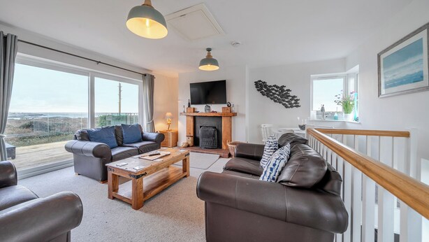 A spacious living room with a fireplace, leather sofas, a wooden coffee table, and large windows offering a view of the landscape. - Curragho (Holyhead)
