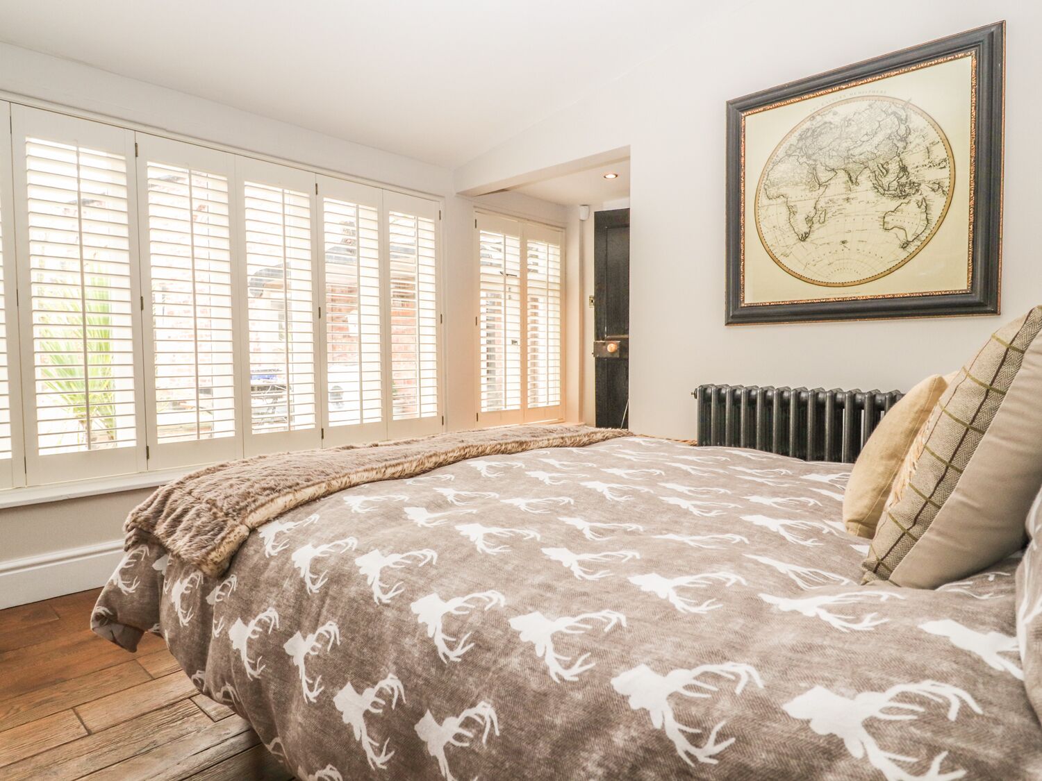 A bedroom with a large bed, a world map on the wall, and a view of the outside through large windows.