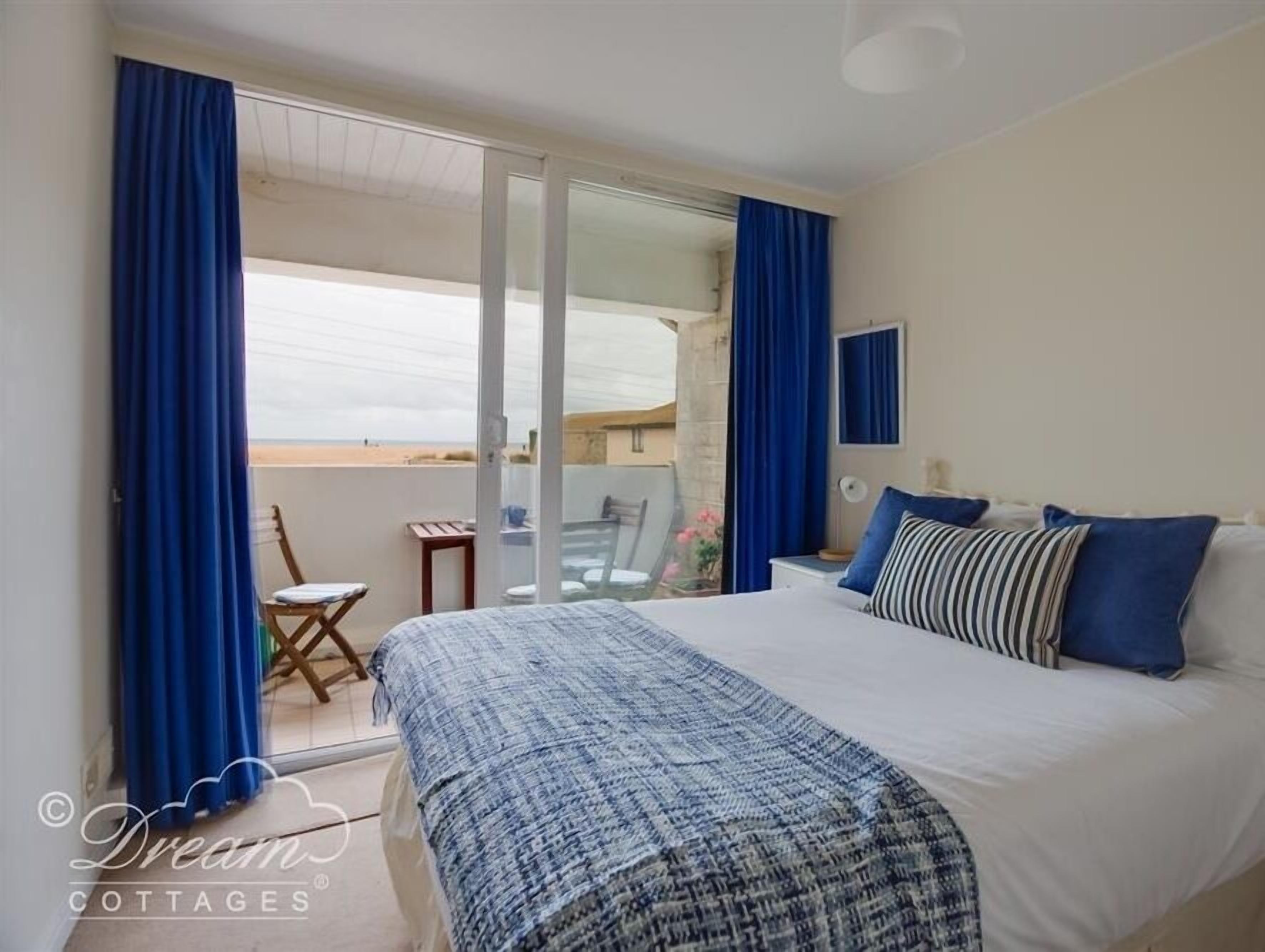 A bedroom with a bed, a chair, a table, and a balcony with curtains.