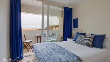 A bedroom with a bed, a chair, a table, and a balcony with curtains.