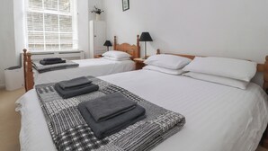 A hotel room with two beds, a window with blinds, a wardrobe, and a small table with a lamp. - 2 Riverside Walk (Skipton)
