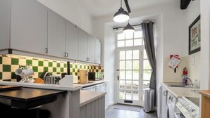 A kitchen with white cabinets, a checkered backsplash, a sink, a stove, and a window with curtains. - 2 Riverside Walk (Skipton)