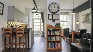 A modern kitchen with wooden chairs, a bookshelf, and a dining area with a black leather sofa. - 2 Riverside Walk (Skipton)