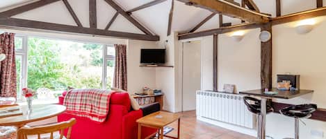 A cozy room with a red sofa, wooden dining table, and a kitchen area with a radiator and bar stools.