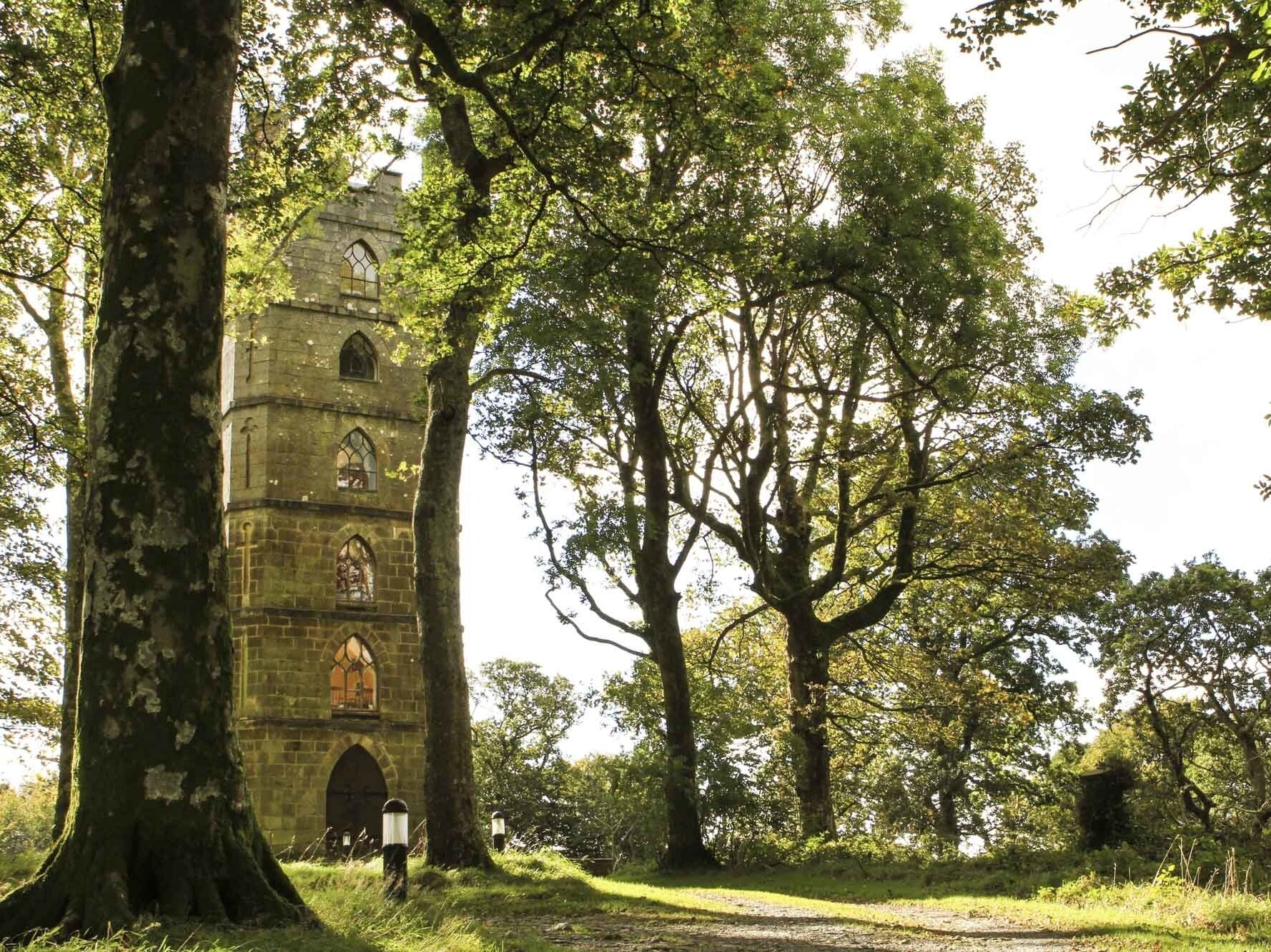 A historic stone tower with arched windows, surrounded by lush greenery and trees.