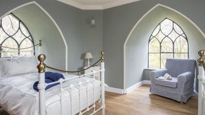 A bedroom with a white metal bed frame, a blue throw blanket, and a checkered armchair. - Brynkir Tower (Garndolbenmaen)
