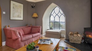 A cozy living room with a pink sofa, a wooden coffee table, a fireplace, and a large arched window. - Brynkir Tower (Garndolbenmaen)