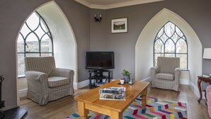 A living room with two armchairs, a wooden coffee table, a television, and large arched windows. - Brynkir Tower (Garndolbenmaen)