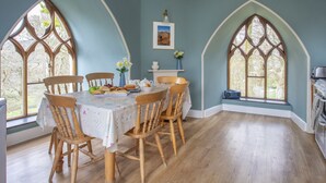 A dining room with a table set for four, surrounded by wooden chairs, large arched windows, and a view of the outdoors. - Brynkir Tower (Garndolbenmaen)