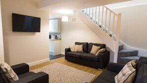A living room with a sofa, a coffee table, and a TV. There is a staircase leading to an upper level. - Hafan (Llangollen)