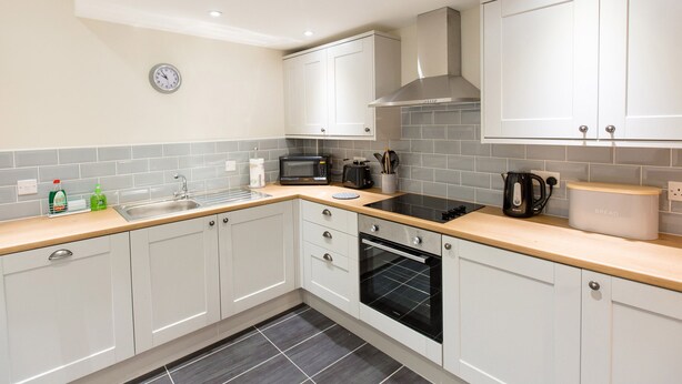 A modern kitchen with white cabinets, a built-in oven, a microwave, and a sink. - Hafan (Llangollen)