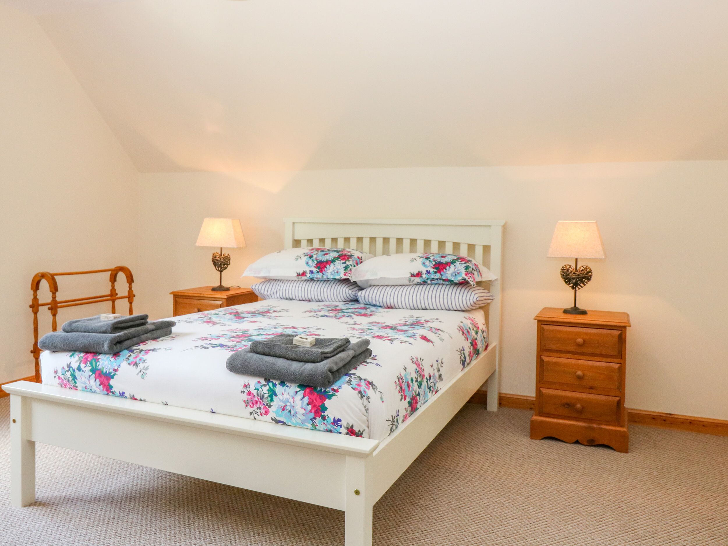 A bedroom with a bed, two bedside tables, a wooden chair, and a carpeted floor.