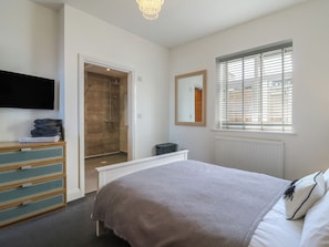 Une chambre à coucher comprenant un lit, une commode, un téléviseur, une douche, une fenêtre avec des stores et un radiateur.