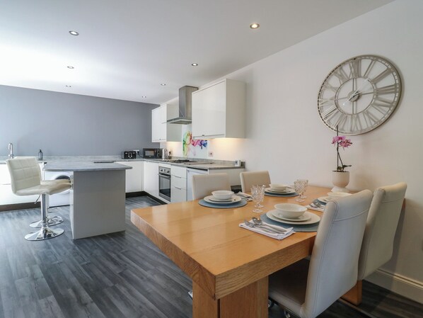 Una cocina moderna con armarios blancos, una mesa de comedor para cuatro personas y un reloj de pared grande.
