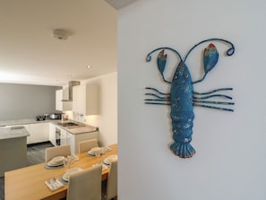Une cuisine moderne avec des meubles blancs, un coin repas doté d’une table en bois pour quatre personnes, et une œuvre d’art murale décorative représentant un homard.