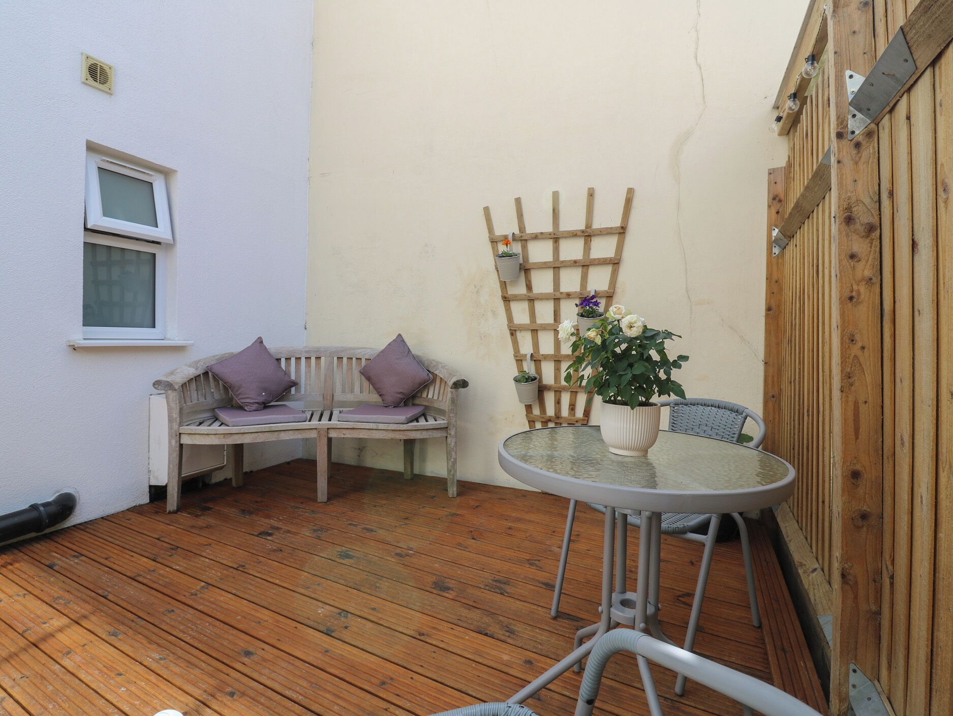 Una terraza de madera con un banco blanco y una mesa redonda con una planta en maceta.