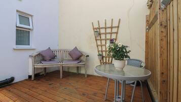 Una terraza de madera con un banco blanco y una mesa redonda con una planta en maceta.