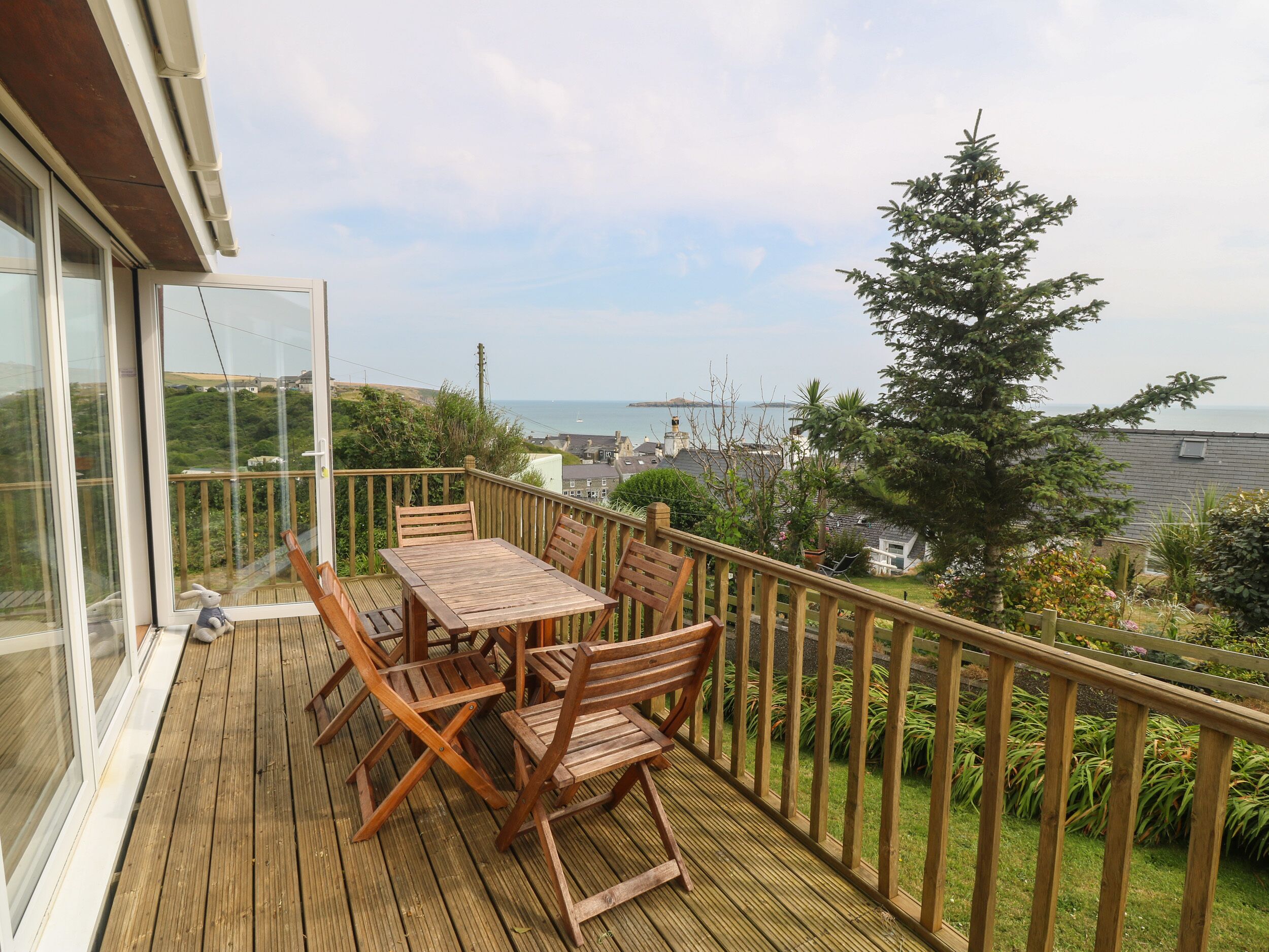 Um deck de madeira com mesa e cadeiras, com vista para a costa, casas e vegetação.