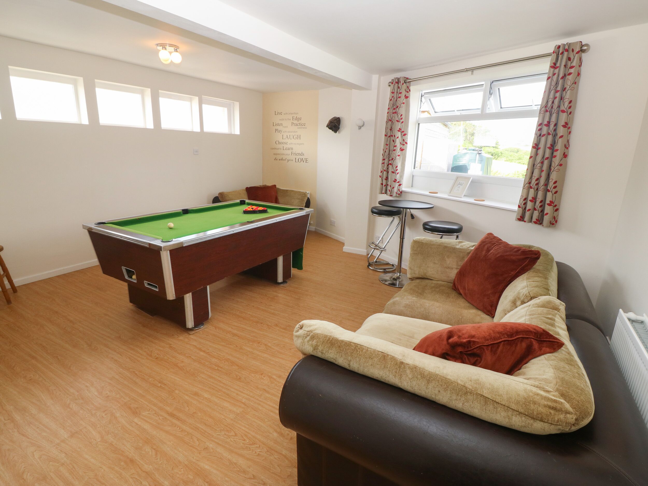 A pool table in a room with a sofa and a window with curtains.