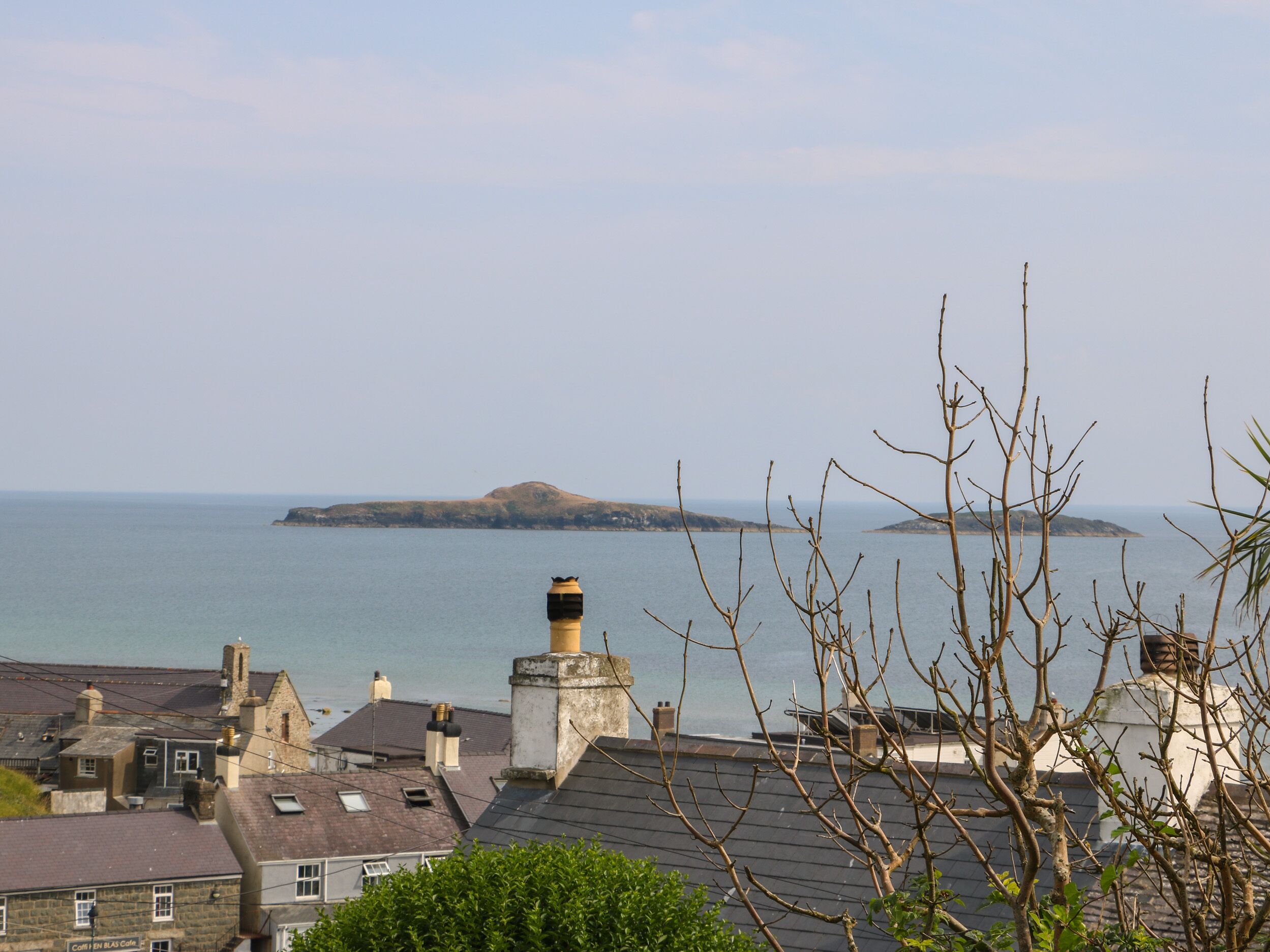 A coastal town with stone buildings, a prominent lighthouse, and a view of the sea and distant island.