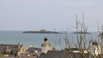 A coastal town with stone buildings, a prominent lighthouse, and a view of the sea and distant island.