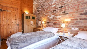 A room with two beds, wooden wardrobe, and brick walls. - The Dairy Barn (Fakenham)