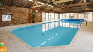 An indoor swimming pool with a stone wall and wooden beams on the ceiling. - The Dairy Barn (Fakenham)