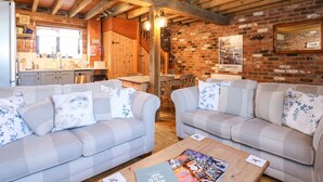 A cozy interior with two sofas, a wooden ceiling, a brick wall, and a kitchen area. - The Dairy Barn (Fakenham)