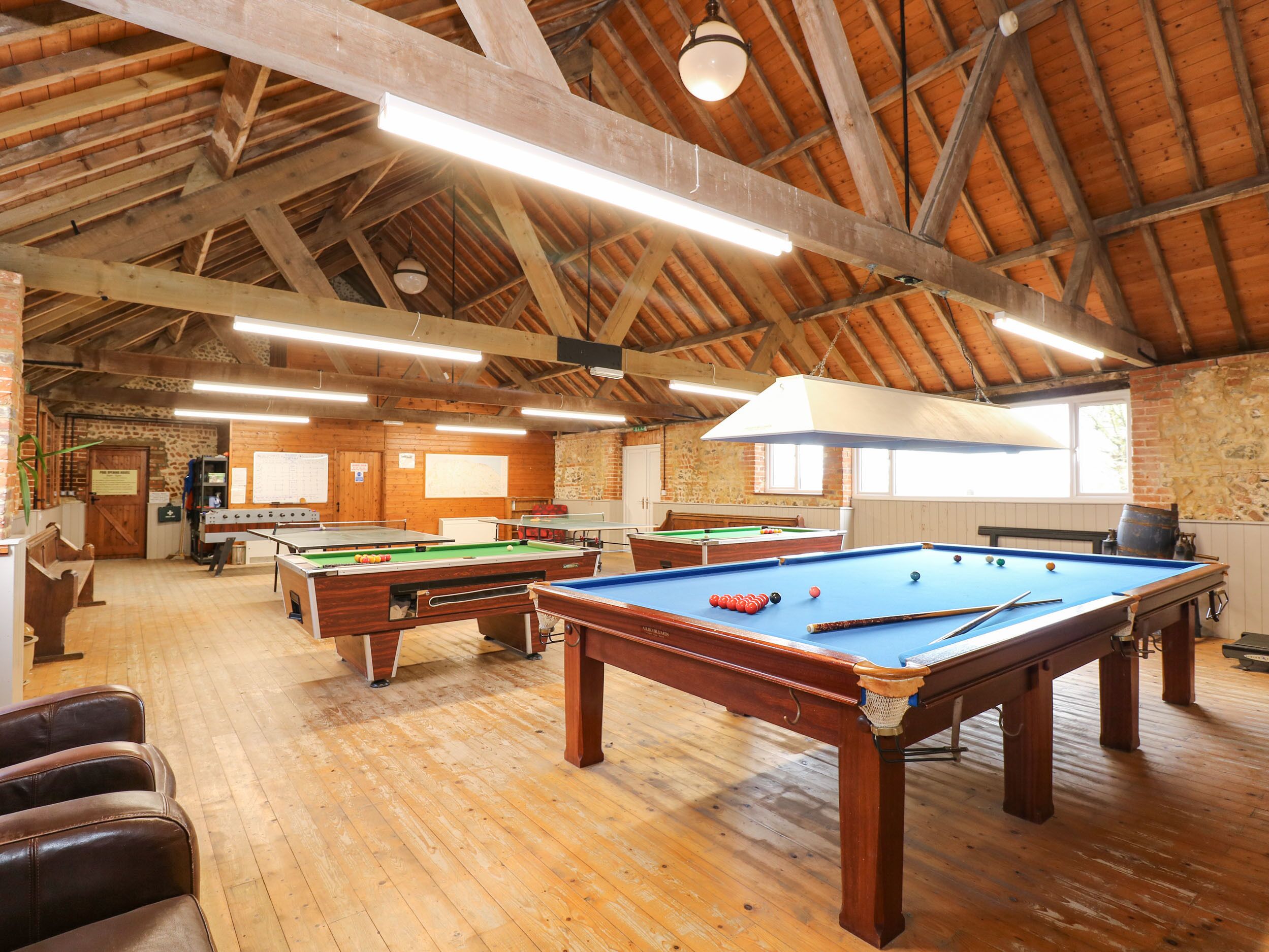 A spacious indoor recreational area with multiple pool tables, wooden flooring, and a high wooden ceiling with exposed beams.